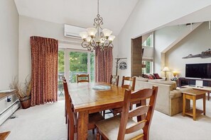 A dining area with a wooden table and chairs, a chandelier, and a view of greenery outside. - Ski-in/out mountainside condo with pool, hot tub, game room & washer/dryer (Ludlow)