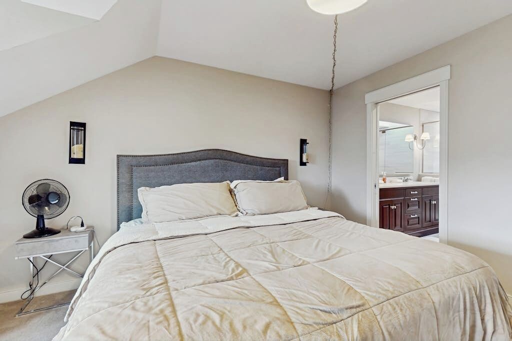 Quarto com cama, mesa de cabeceira, ventilador e espelho.