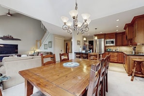 A spacious dining area with a wooden table and chairs, a chandelier, and a kitchen with wooden cabinets and appliances. - Ski-in/out mountainside condo with pool, hot tub, game room & washer/dryer (Ludlow)