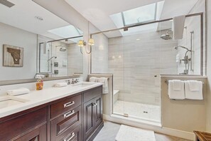Un baño moderno con tragaluz, ducha envuelta en cristal y un espejo grande.
