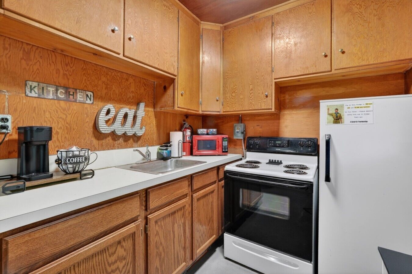 A compact kitchen with wooden cabinets, a white countertop, a coffee maker, a microwave, and a stove.