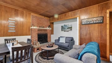 A cozy living room with a brick fireplace, a sofa, a coffee table, and a dining area with a table and chairs.