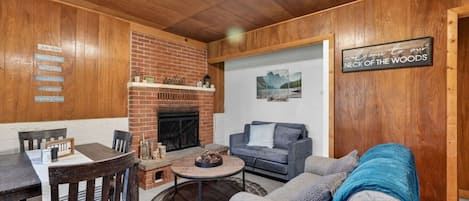 A cozy living room with a brick fireplace, a sofa, a coffee table, and a dining area with a table and chairs.