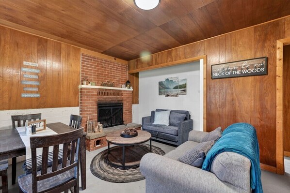 A cozy living room with a brick fireplace, a sofa, a coffee table, and a dining area with a table and chairs.