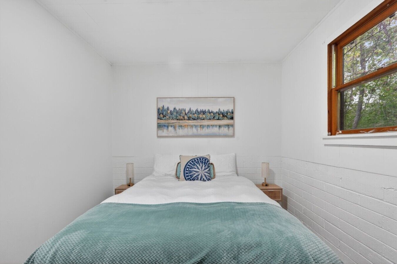 A bedroom with a bed, a painting, a window, and a nightstand.