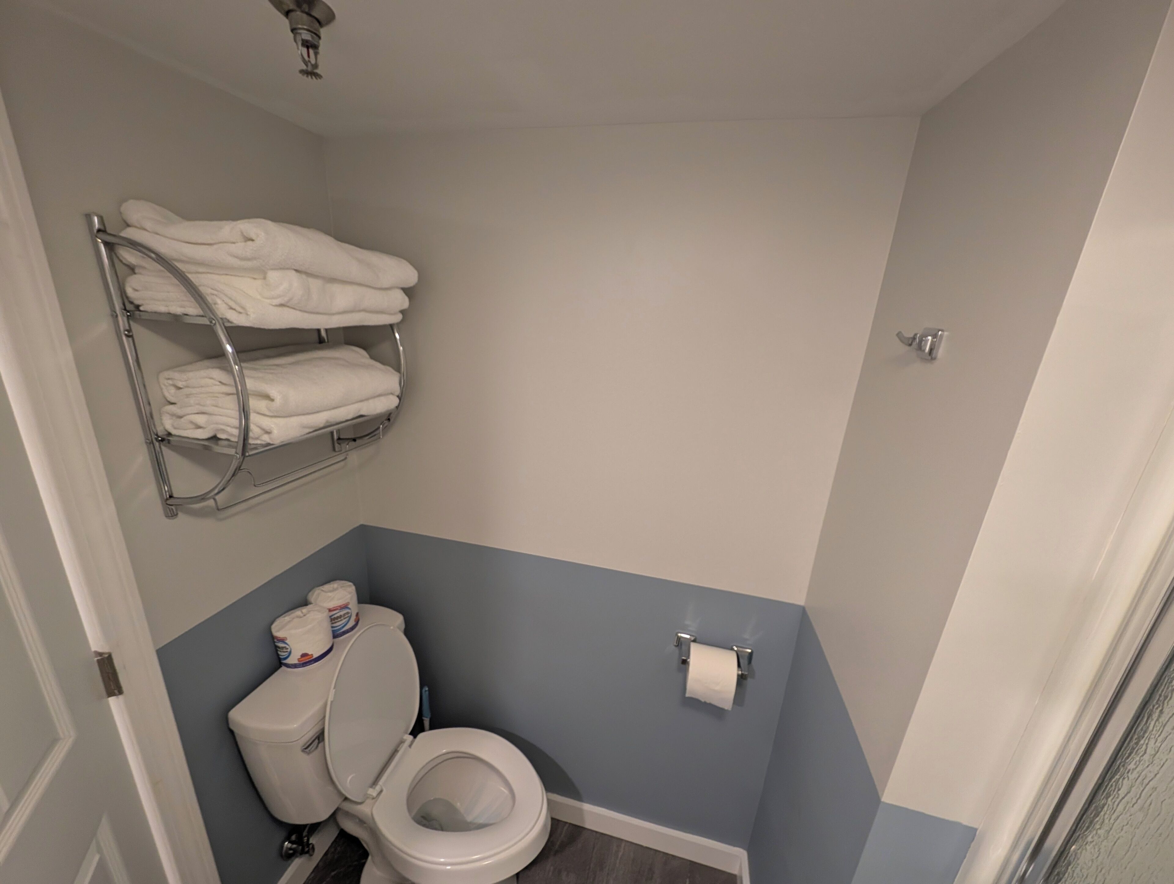 Un baño con inodoro, toallero con toallas dobladas y dispensador de papel higiénico.