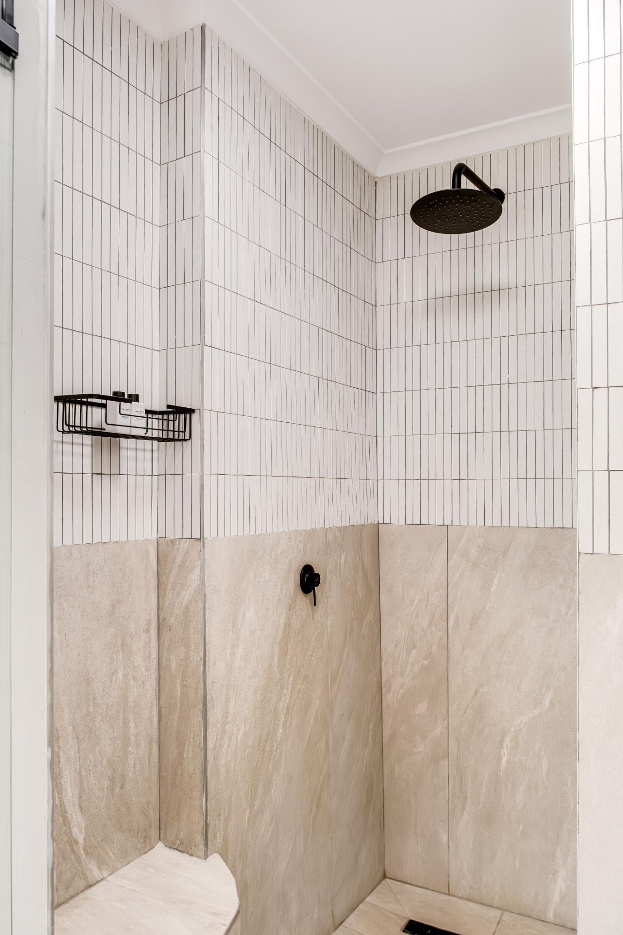 A corner shower with a black showerhead, tiled walls, and a beige floor.