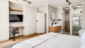 Ein modernes Schlafzimmer mit einem Bett, einem Fernseher, einem Spiegel und einem durch eine offene Tür einsehbaren Badezimmer.