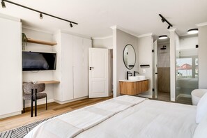 Ein modernes Schlafzimmer mit einem Bett, einem Fernseher, einem Spiegel und einem durch eine offene Tür einsehbaren Badezimmer.
