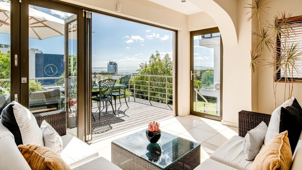 Ein modernes Wohnzimmer mit einem Glastisch, einer Couch und Blick auf einen Balkon mit Gartenmöbeln.