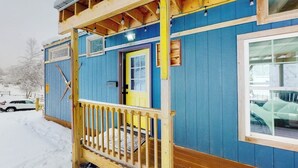 Eine blaue Holzhütte mit gelber Tür, einer Holzterrasse und einem Fenster.