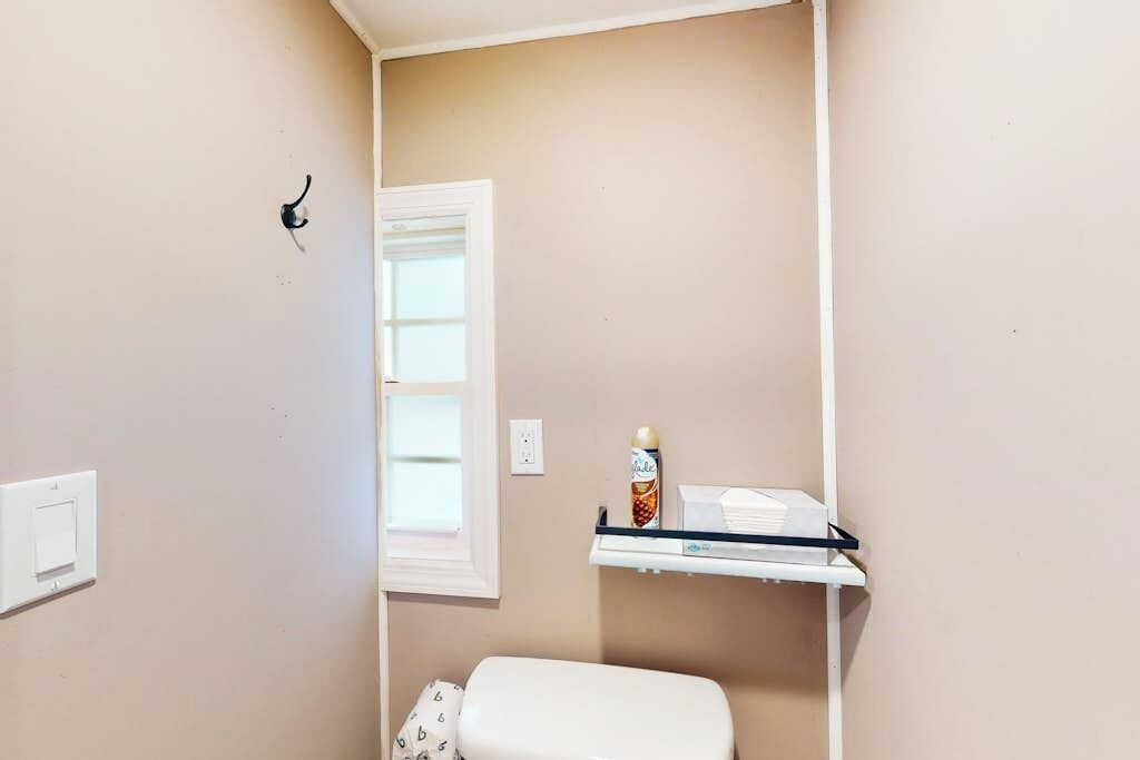 Ein Badezimmer mit Toilette, Ablagefläche für Toilettenartikel, Fenster und Lichtschalter.