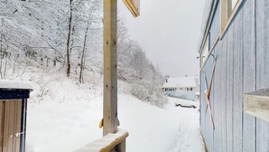 Eine mit Schnee bedeckte Holzterrasse, die zu einem Haus mit blauer Fassade führt.