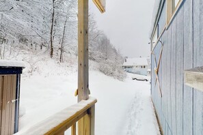 A snow-covered wooden deck leading to a house with a blue exterior. - Two cozy tiny homes with a private hot tub, large deck, grill, AC - dog friendly (Ludlow)