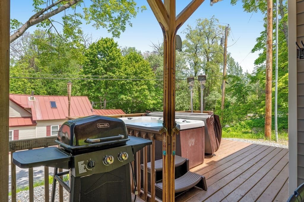 A deck with a grill, hot tub, and wooden deck.