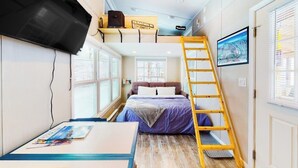 Ein Schlafzimmer im Loft-Stil mit einem Etagenbett, einer Leiter, einem Wand-Fernseher und einem Fenster mit Jalousien.