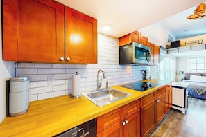 A modern kitchen with wooden cabinets, a stainless steel sink, a microwave, and a dishwasher. - Two cozy tiny homes with a private hot tub, large deck, grill, AC - dog friendly (Ludlow)