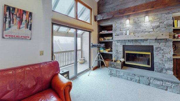 A living room with a stone fireplace, a red leather couch, and a large window.