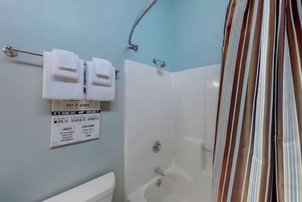 Un baño con ducha, un perchero con dos toallas y un cartel con instrucciones.