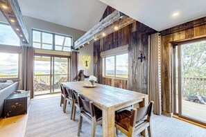 Ein Essbereich mit Holztisch und -stühlen, großen Fenstern mit Aussicht und rustikaler Wandgestaltung.