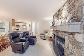 A living room with a fireplace, leather recliners, a kitchen in the background, and a stone accent wall.