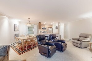 A living room with a dining area, two leather recliners, a beige armchair, and a kitchen in the background.