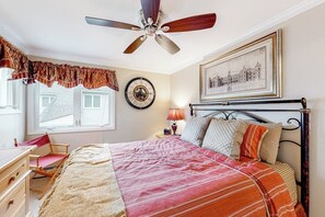 A bedroom with a bed, a desk, a chair, a ceiling fan, a clock, a lamp, and a framed picture on the wall.