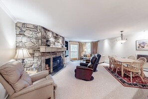 A living room with a stone fireplace, leather recliner, dining table with chairs, and a chandelier.