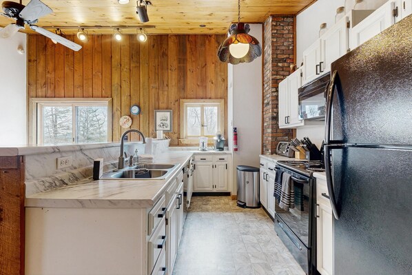 Una cocina moderna con paredes de madera, encimera de mármol, refrigerador negro y estufa.