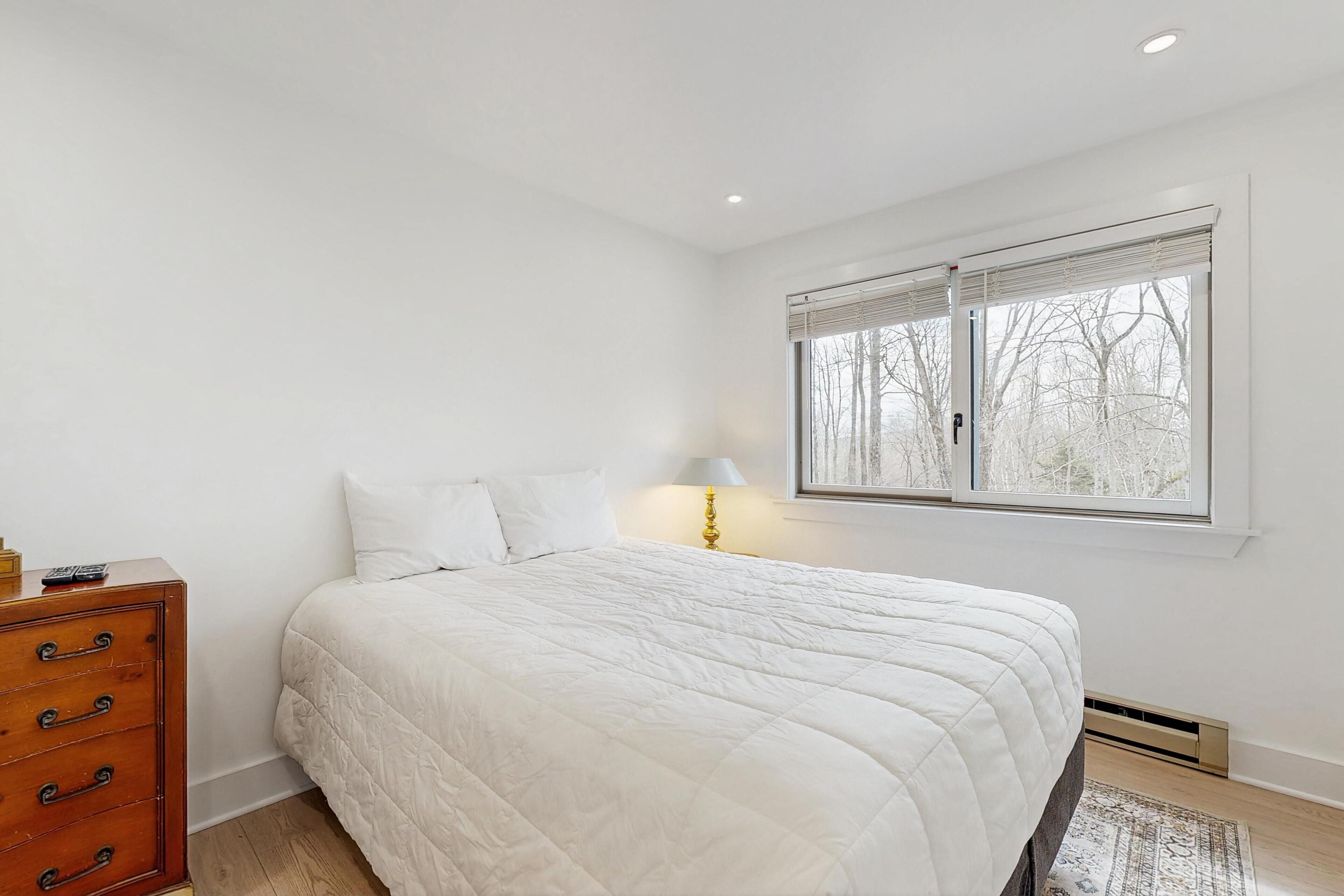 Une chambre à coucher avec un lit, une commode, une fenêtre avec des stores et une lampe.