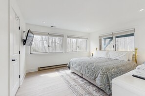Un dormitorio con cama, televisor montado en la pared y ventana con persianas.