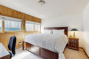 A bedroom with a wooden headboard, a bed with white bedding, a bedside table with a lamp, and a chair. - Three-story Ludlow Mountain home with private hot tub, firepit and EV charger (Ludlow)