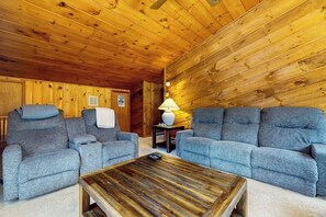 Ein gemütlicher Raum mit Holzwänden und -decken, zwei grauen Sofas, einem Holztisch und einem kleinen Tisch mit einer Lampe.
