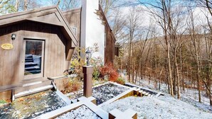 Una cabaña de madera con chimenea, una puerta con placa de número y un paisaje cubierto de nieve.