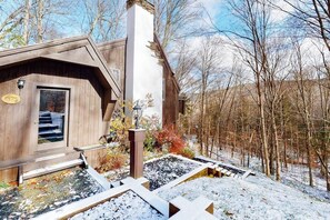A wooden cabin with a chimney, a door with a number plate, and a snow-covered landscape. - Rustic home with a private hot tub, cable, & washer/dryer (Plymouth)