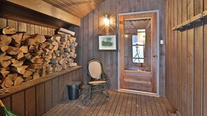 Un interior de madera con leña apilada, una silla y una puerta que da a otra habitación.