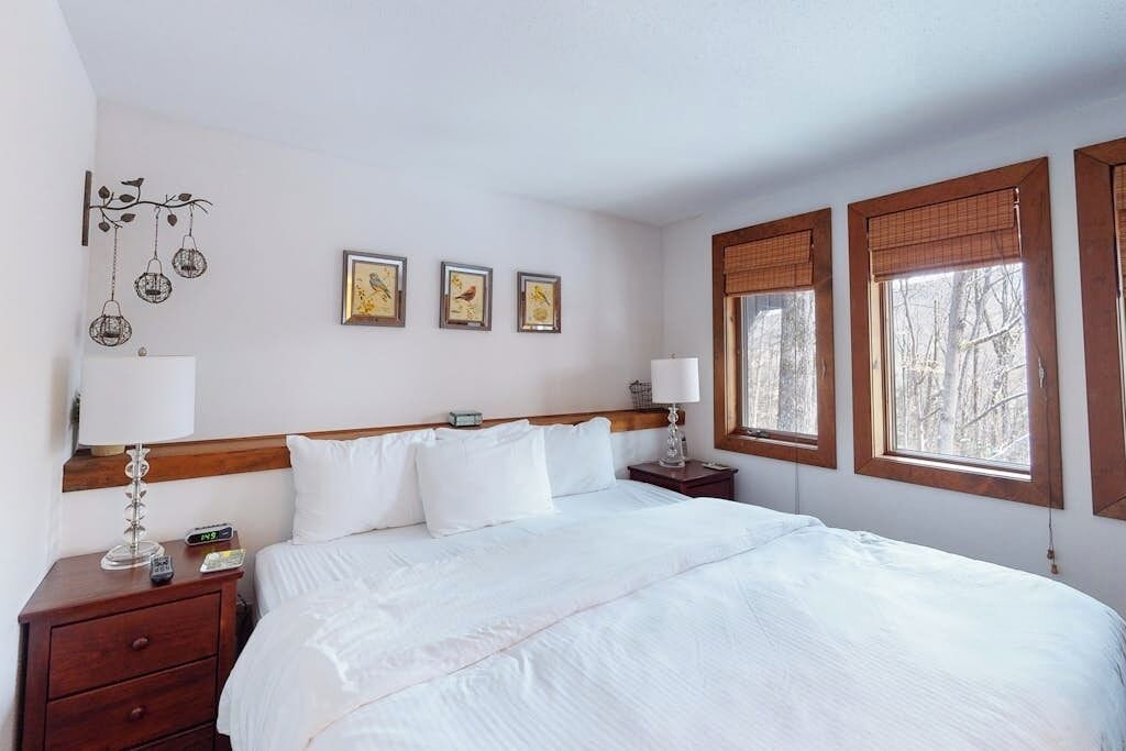 Une chambre à coucher avec un lit, des tables de chevet, des œuvres d’art murales et des fenêtres.