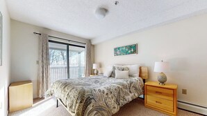 Ein Schlafzimmer mit einem Bett, einem Nachttisch, einer Lampe, einem Gemälde und einer Schiebetür zum Balkon.