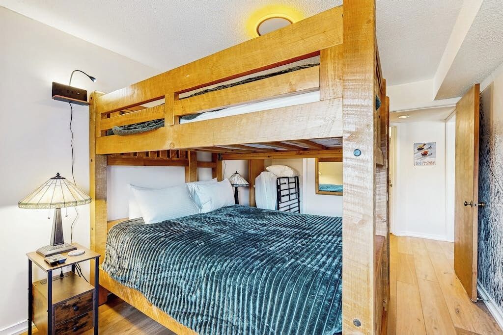 A bunk bed room with a wooden headboard, a bedside table with a lamp, and a poster on the wall.