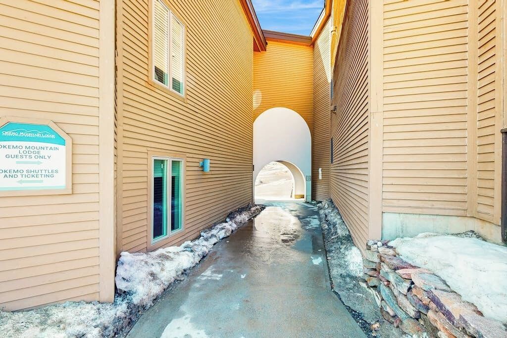 A narrow corridor with wooden walls, a stone wall on one side, and a sign indicating a mountain lodge.