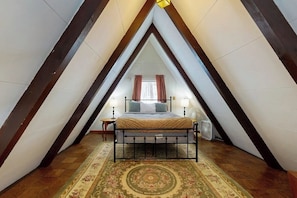 Ein Schlafzimmer mit schrägem Dach, einem Bett, einem Nachttisch und einem Ventilator.