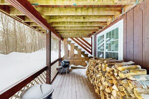 Eine überdachte Veranda mit Holzgeländer, Grill und Holzstapel.