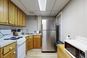 A kitchen with wooden cabinets, a stainless steel refrigerator, a stove, and a microwave. - Cozy duplex, first floor unit w/ kitchen, shared fire pit, lake access, wifi, TV (Ludlow)