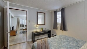 A bedroom with a bed, a desk, a mirror, and a door leading to another room. - Cozy duplex, first floor unit w/ kitchen, shared fire pit, lake access, wifi, TV (Ludlow)