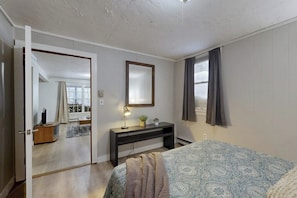 A bedroom with a bed, a desk, a mirror, and a door leading to another room. - Cozy duplex, first floor unit w/ kitchen, shared fire pit, lake access, wifi, TV (Ludlow)