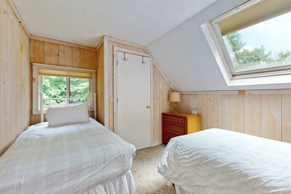 Ein Schlafzimmer mit zwei Betten, einem Fenster, einer Tür und einem Nachttisch.