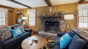 A cozy living room with a fireplace, wooden walls, and two sofas with patterned cushions.