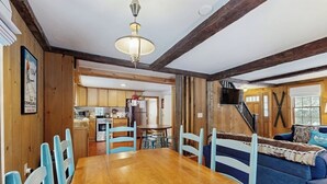 A dining area with a wooden table and blue chairs, a kitchen in the background, and a staircase leading to another level.
