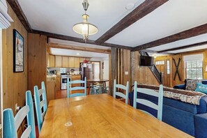 A dining area with a wooden table and blue chairs, a kitchen in the background, and a staircase leading to another level.