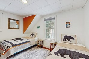 A bedroom with two beds, a window, a mirror, and a door.